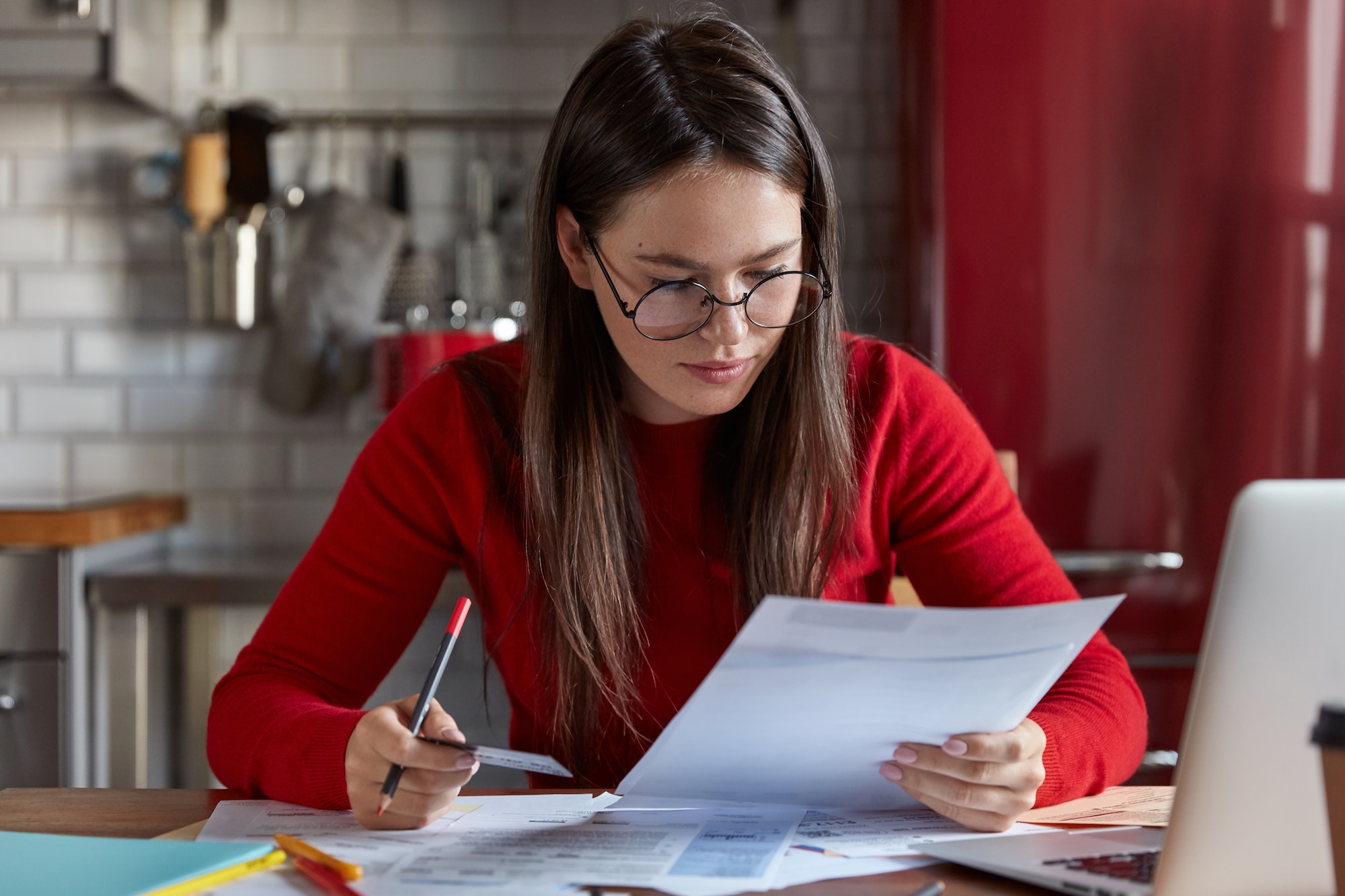 Indoor shot of woman financier in optical glasses checks bank account, recieves bills, holds plastic