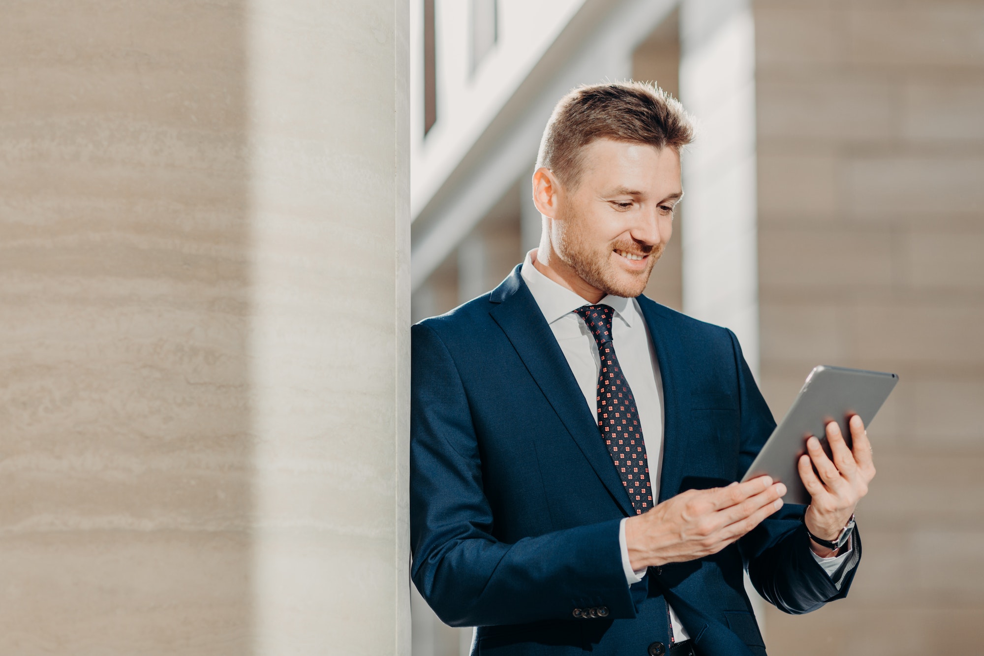 Professional male CEO in elegant suit, checks banking account on tablet in internet