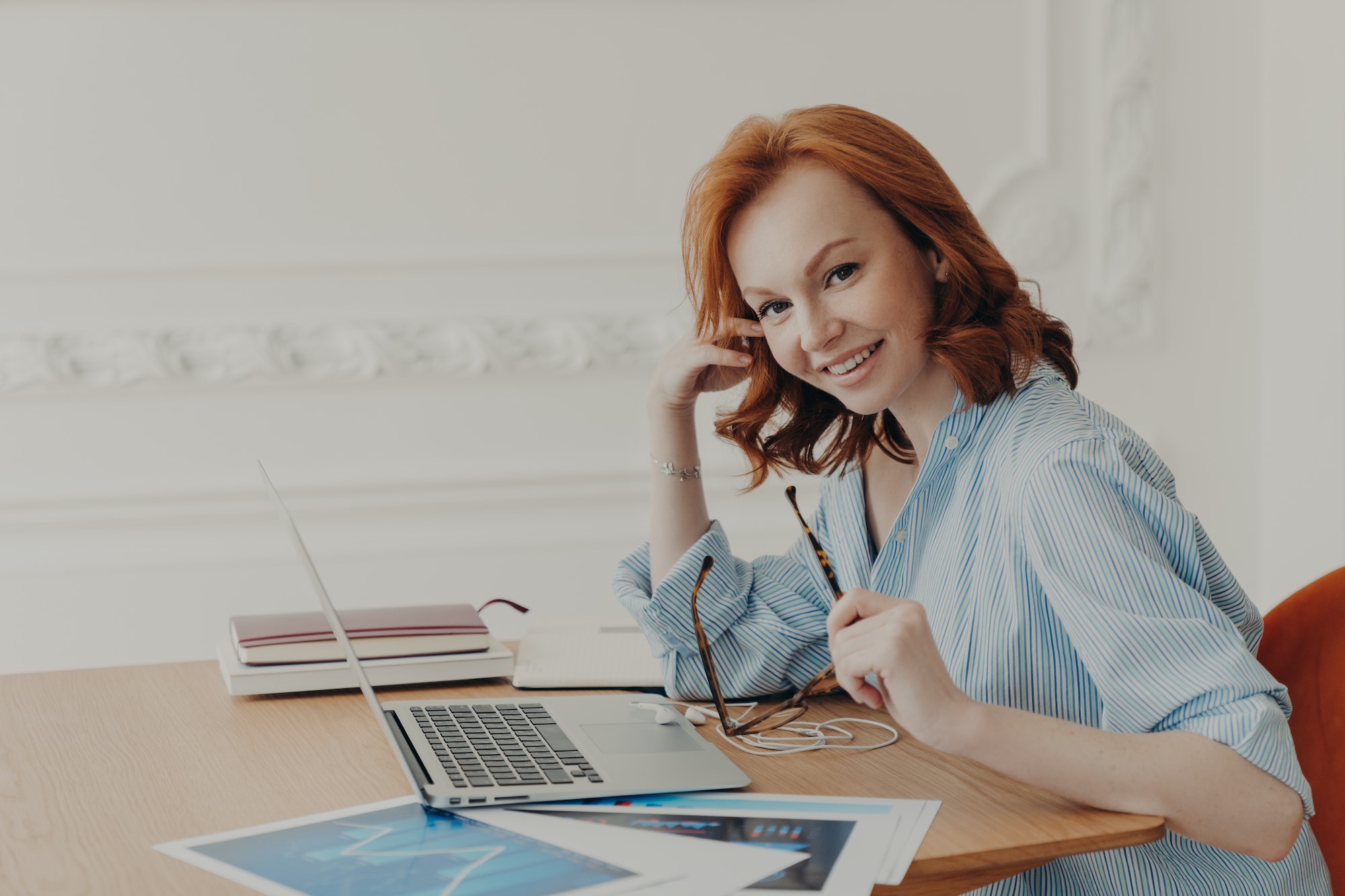 Satisfied businesswoman with foxy hair, checks accounting documentation in online database